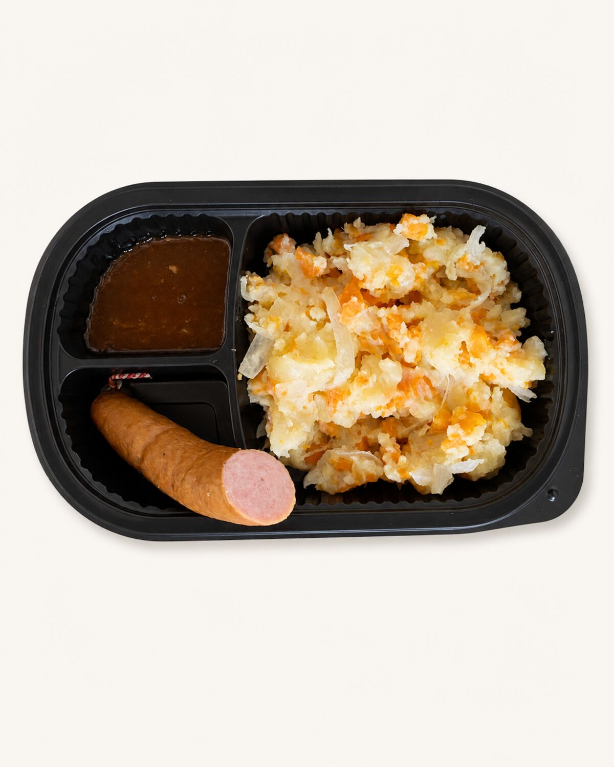 Maaltijdbak met hutspot van gestampte aardappel, wortel en ui, met een rookworst erbovenop en jus over de stamppot.
